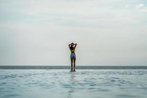 aziatische thaise tiener vrouw in geel ontspannen en zwemmen pak is posten op de infinity pool naast de zee strand in thailand resort. foto