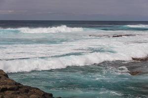 turbulente oceaangolven met wit schuim slaan kuststenen foto