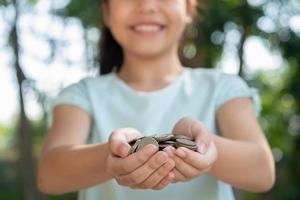 schattig Aziatisch meisje dat met munten geld speelt, kind hand met geld. kind spaart geld in spaarvarken. kind telt zijn gespaarde munten, kinderen leren over voor het toekomstige concept. foto