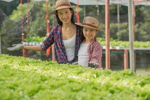 Aziatische moeder en dochter helpen samen bij het verzamelen van de verse hydrocultuurgroente op de boerderij, concepttuinieren en kindereducatie van huishoudelijke landbouw in gezinslevensstijl. foto