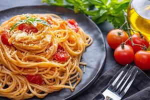 smakelijke smakelijke klassieke italiaanse spaghetti pasta met tomatensaus, kaas Parmezaanse kaas en basilicum op plaat en ingrediënten voor het koken van pasta op donkere tafel. foto