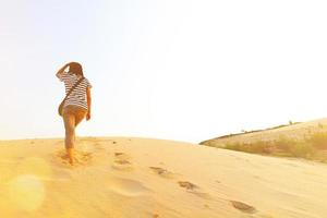 aziatische vrouw die door de woestijn loopt met veel voetafdruk op het zand met zonlicht flare en kopieer ruimte in sam phan bok, ubonratchathani, thailand. mensen noemen de Grand Canyon van Thailand en de beroemde plaats foto