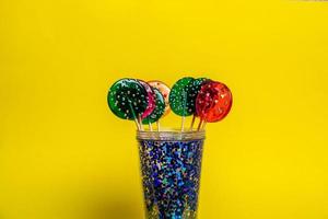 veelkleurige lolly's in een blauw glas op een gele achtergrond. foto