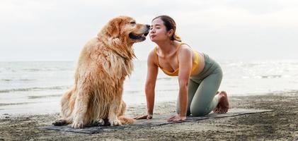 Aziatische jonge vrouw kust haar hond tijdens het doen van yoga op een yogamat op het strand. ontspanning met een huisdier. foto