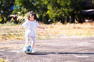 portretbeelden Aziatisch meisje 5 jaar oud. actief kind voetballen in betonnen veld. gelukkig kind met sportactiviteiten concept. lege ruimte voor het invoeren van tekst. kleine atleet die graag traint. foto