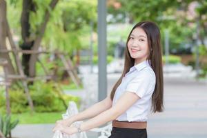 portret van een volwassen thaise student in universitair studentenuniform. Aziatische mooi meisje zit gelukkig lachend aan de universiteit met een achtergrond van tuin bomen. foto