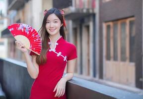 mooie aziatische vrouw in rode jurk staat met een ventilator in het oude stadscentrum in het thema van het chinees nieuwjaar. foto