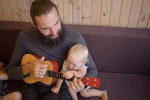 bebaarde vader met kinderen spelen op ukelele indoor foto