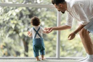 schattig peuter klein kind familieconcept, baby leert lopen met vader en moeder om te helpen zorgen en hand vast te houden, eerste stap met ouderondersteuning uit de kindertijd, klein liefdesportret jongetje thuis foto