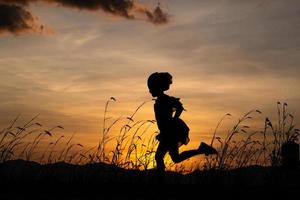 silhouet van kind meisje draait op de weide bij zonsondergang achtergrond. foto