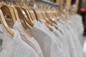 witte kleren die op houten rekken hangen. kleding voor vrouwen die aan hangers hangen in het winkelcentrum te koop. foto