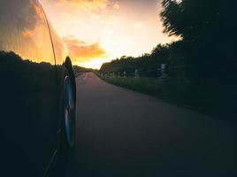 fast motion auto wiel draait snel op asfaltweg met herfst natuur bomen en landschap op kronkelige weg. reizen in een rustige zomeravond en road trip concept. opzettelijk vervagen filter effect foto