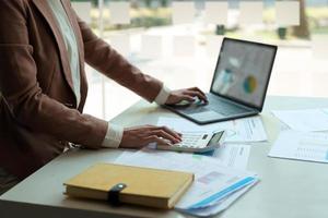 close-up van een accountant die bezig is met financiën met rekenmachine en laptopcomputer op kantoor om uitgaven te berekenen, boekhoudconcept foto