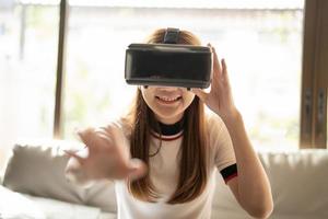 prikkel aziatische vrouw die online game speelt met vr-bril en controller bij haar thuis foto