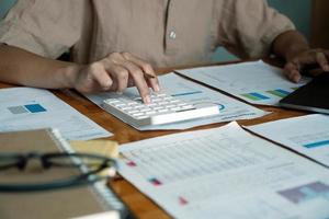 Close-up van zakenvrouw of accountant hand met pen bezig met rekenmachine om bedrijfsgegevens, boekhouddocument en laptopcomputer op kantoor, bedrijfsconcept te berekenen foto