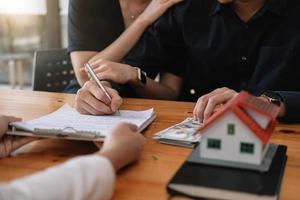 makelaar biedt hand voor klant teken overeenkomst contract handtekening voor koop of verkoop huis. gelukkig Aziatisch paar dat samen een contract ondertekent op kantoor. onroerend goed contact overeenkomst concept foto