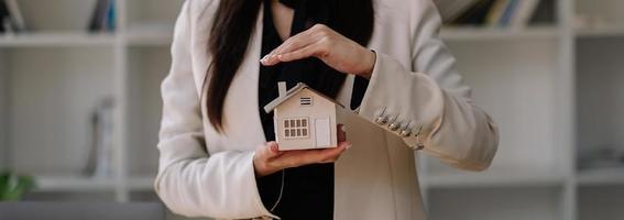 huis bedekt met handen van de vrouw - verzekering onroerend goed concept. foto