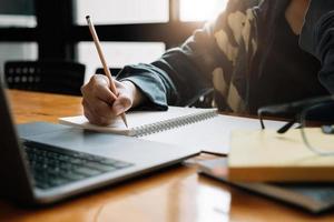 bijgesneden foto van Aziatische vrouw schrijven lijst maken van notities in Kladblok werken of leren op laptop binnenshuis-educatieve cursus of training, seminar, onderwijs online concept