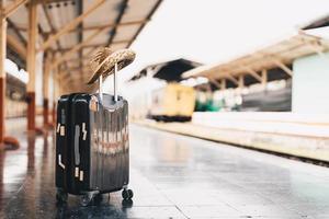 zomer reisconcept bagage met strohoed op treinstation in de buurt van spoorweg. foto