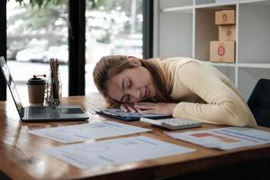 jonge aantrekkelijke aziatische zakenvrouw slapen, dutten of een dutje doen aan haar bureau, vermoeide accountant met financiële papieren mappen op kantoor foto