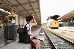 jonge vrouw reiziger met rugzak op zoek naar kaart tijdens het wachten op trein, aziatische backpacker op perron op treinstation. vakantie, reis, reis en zomer zomer reisconcept foto