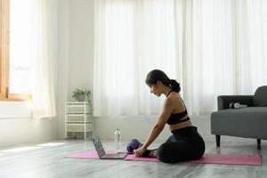 fit sportieve jonge aziatische vrouw online training oefening thuis. actieve gezonde meid geniet van sport pilates yoga fitness training op laptop computer die zich uitstrekt op yoga mat kijken naar video klasse foto