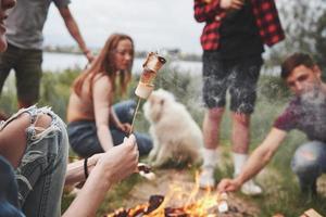 geroosterde marshmallow in camerafocus. groep mensen hebben picknick op het strand. vrienden veel plezier in het weekend foto