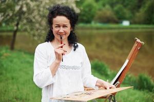 plezier hebben tijdens het proces. portret van volwassen schilder met zwart krullend haar in het park buiten foto