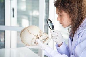jonge mooie wetenschapper arts of onderzoeker onderzoekt en bestudeert schedel in laboratorium. foto