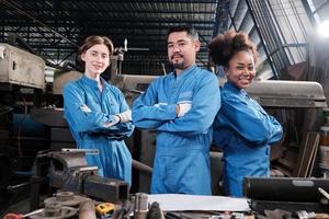 multiraciale industriearbeiders in veiligheidsuniformen werken samen met eenheid, armen gekruist en drukken gelukkig werk uit samen met een glimlach en vrolijk in mechanische fabriek, professionele ingenieursbezetting. foto