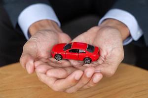 zakenman hand met rode auto speelgoed op tafel. financieel, geld, herfinancieren en autoverzekeringsconcept foto