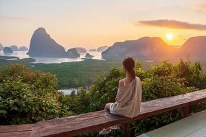 gelukkige reiziger vrouw geniet van phang nga baai uitkijkpunt, alleen toerist zit en ontspant in samet nang she, in de buurt van phuket in het zuiden van thailand. Zuidoost-Azië reizen, reis en zomervakantie concept foto