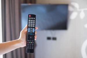 hand met afstandsbediening voor het aanpassen van smart tv in de moderne kamer thuis of in een luxe hotel foto