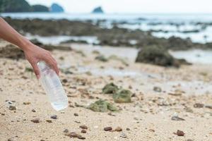 vrijwilliger hand ophalen van afval, plastic fles afval op het strand. ecologie, milieu, vervuiling en ecologisch probleemconcept foto