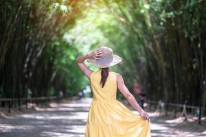 aziatische vrouw in gele jurk en hoed die op groene bamboetunnel reist, gelukkige reiziger die de chulabhorn-wanaram-tempel loopt. mijlpaal en populair voor toeristenattracties in nakhon nayok, thailand foto