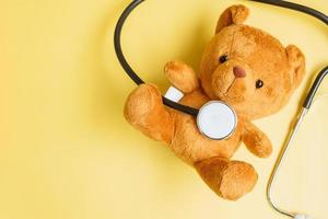 stethoscoop met berenpop op gele achtergrond voor het ondersteunen van het leven en de ziekte van kinderen. september bewustzijnsmaand voor kinderkanker, concept voor gezondheidszorg en levensverzekeringen foto