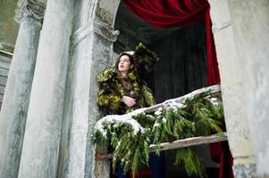 brunette meisje in groene bontjas tegen oude boog met kolommen en rode gordijnen. foto