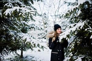 mooie brunette meisje in warme winterkleding. model op winterjas en muts in de buurt van pijnbomen. foto