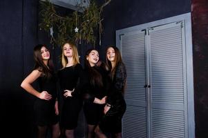 vier schattige vriendenmeisjes dragen zwarte jurken tegen kerstversiering. foto
