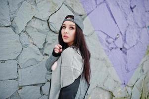 stijlvolle brunette meisje in grijze pet, casual straatstijl op winterdag tegen gekleurde muur. foto