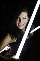 krullend brunette plus size model met twee lange led-lampen op zwarte kamer. foto