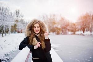 mooie brunette meisje in warme winterkleding. model op winterjas tegen bevroren meer in het park. foto