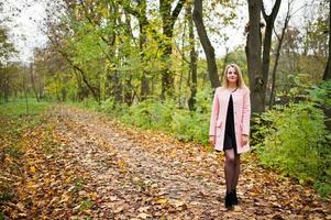 jong blond meisje met roze jas gesteld op herfst park. foto