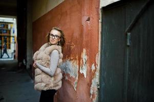 blond meisje op bontjas en bril poseerde tegen oude oranje muur. foto