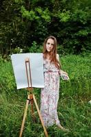 portret van een aantrekkelijke jonge vrouw in lange jurk schilderen met waterverf in de natuur. foto
