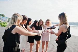 groep van 8 meisjes dragen op zwart en 2 bruiden op vrijgezellenfeest tegen zonnig strand champagne drinken. foto