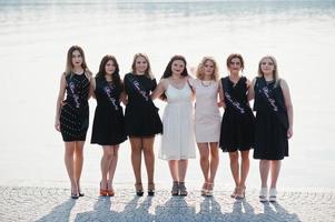 groep van 7 meisjes dragen op zwart en 2 bruiden op vrijgezellenfeest tegen zonnig strand. foto