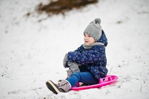 schattig klein meisje met schotel sleeën buiten op winterdag. foto