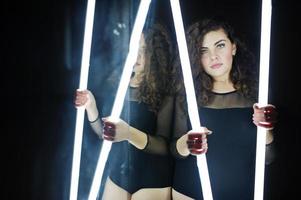 krullend brunette plus size model met twee lange led-lampen in de dansruimte met spiegel. foto