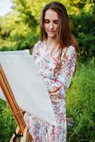 portret van een aantrekkelijke jonge vrouw in lange jurk schilderen met waterverf in de natuur. foto